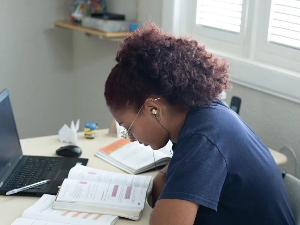 Estudante da Segunda chamada estudando em casa, com livros, cadernos e notebook sobre a mesa